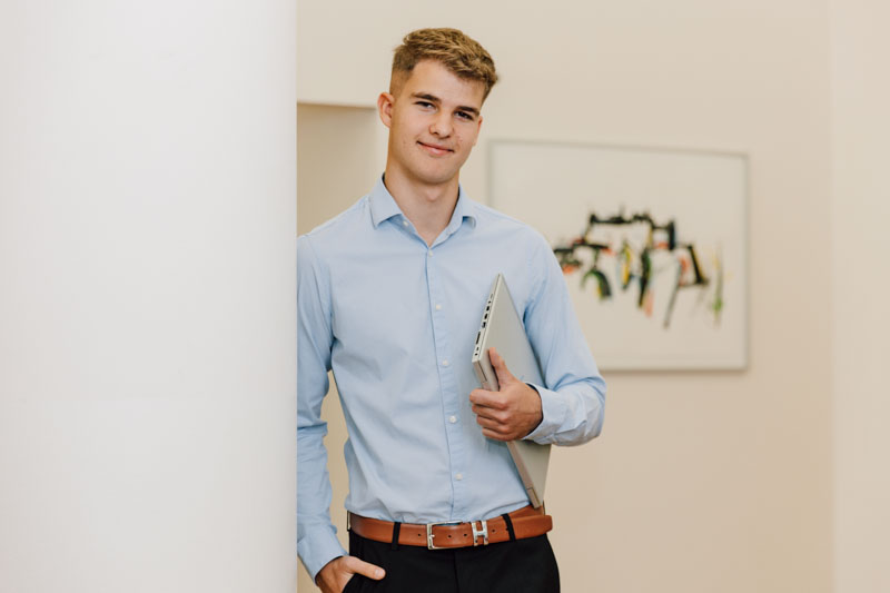 Lehrling lehnt an der Wand mit Laptop in der Hand